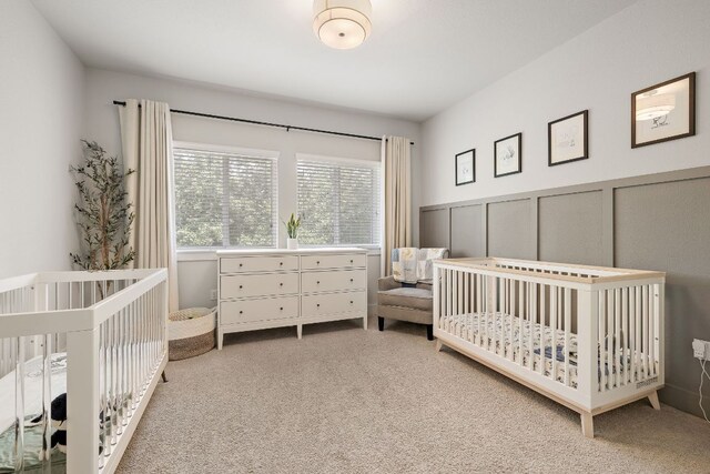 carpeted bedroom with wainscoting, a decorative wall, and a nursery area