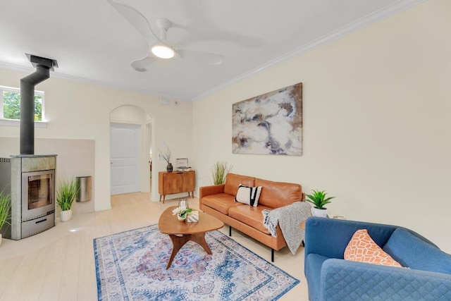 living area featuring arched walkways, ornamental molding, a ceiling fan, and a wood stove