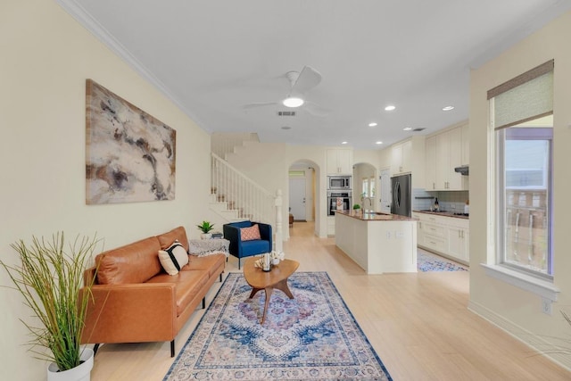 4128 E Lawless St, Austin, TX 78723 - living room featuring arched walkways, stairway, light wood-style floors, a ceiling fan, and crown molding