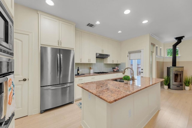 4128 E Lawless St, Austin, TX 78723 - kitchen featuring appliances with stainless steel finishes, under cabinet range hood, light wood finished floors, decorative backsplash, and light stone counters