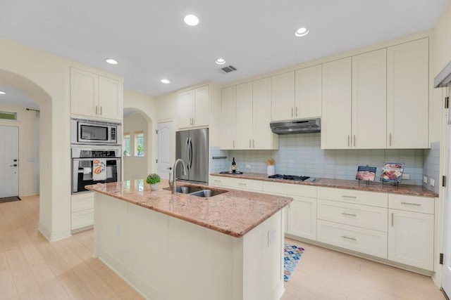 kitchen with a sink, appliances with stainless steel finishes, under cabinet range hood, and arched walkways