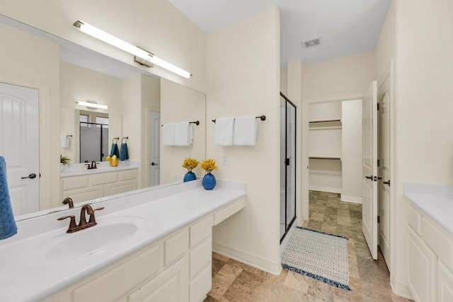 bathroom with a walk in closet, visible vents, a shower stall, vanity, and baseboards