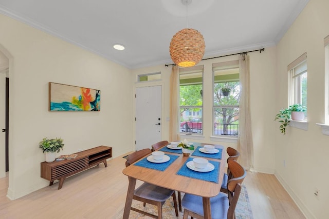 dining space featuring arched walkways, baseboards, ornamental molding, and light wood-type flooring