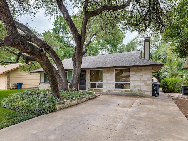 ranch-style home with concrete driveway, roof with shingles, a chimney, and stone siding