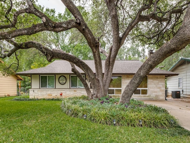 view of front of home featuring a shingled roof, cooling unit, a front lawn, and stone siding