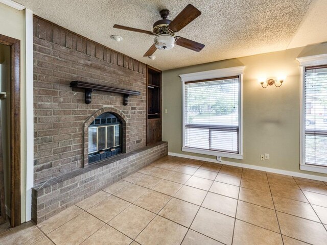 unfurnished living room with light tile patterned floors, a ceiling fan, a brick fireplace, and a textured ceiling