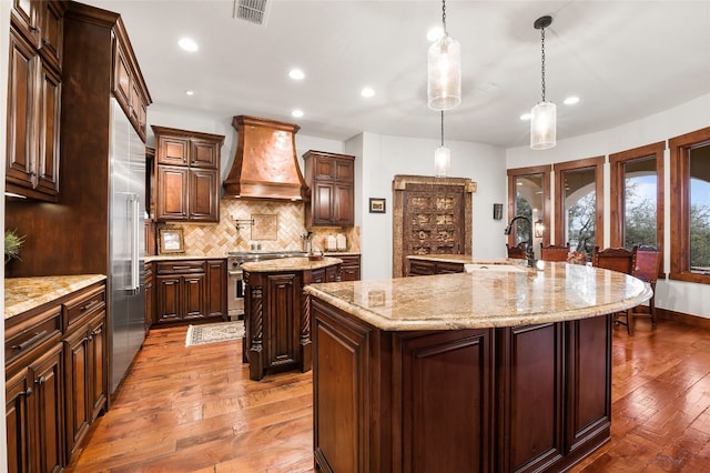 kitchen featuring visible vents, high end appliances, a large island, premium range hood, and a sink