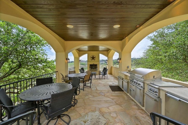 view of patio with exterior kitchen, area for grilling, outdoor dining area, exterior fireplace, and a sink
