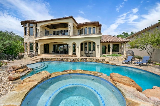 rear view of property featuring a ceiling fan, a tile roof, a pool with connected hot tub, a patio area, and a balcony