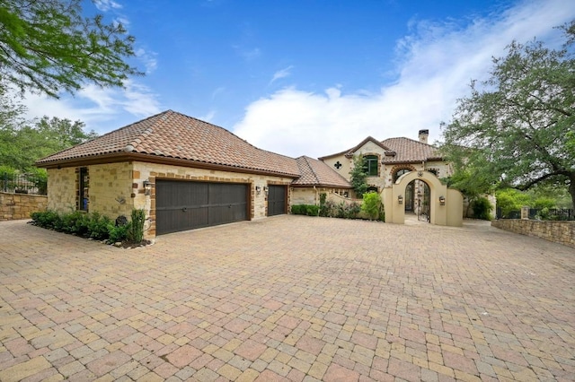 view of front of property with stone siding, a chimney, a tiled roof, an attached garage, and driveway