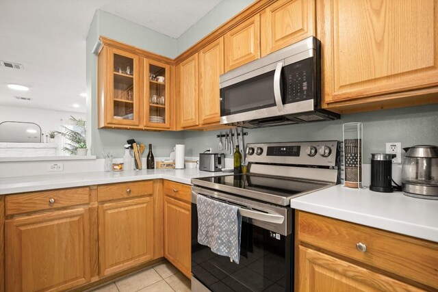kitchen featuring visible vents, light tile patterned floors, light countertops, glass insert cabinets, and stainless steel appliances