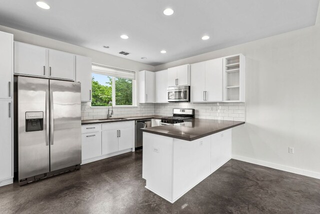 kitchen featuring finished concrete flooring, appliances with stainless steel finishes, dark countertops, a sink, and a peninsula