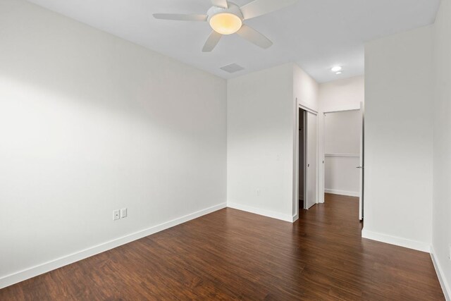empty room with baseboards, ceiling fan, visible vents, and dark wood-type flooring