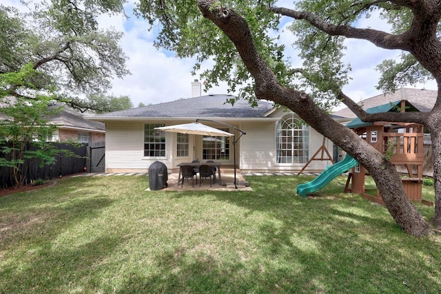 rear view of house with fence, a patio, a chimney, a playground, and a yard