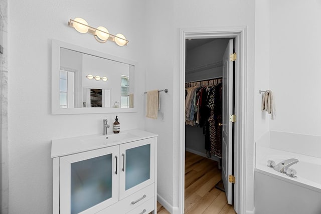 bathroom with vanity, a walk in closet, a garden tub, and wood finished floors