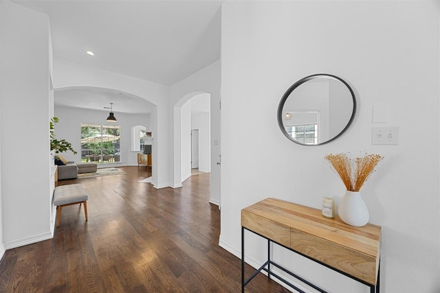 corridor featuring arched walkways, baseboards, and wood finished floors