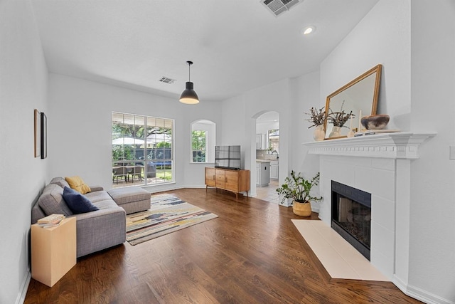 living room with visible vents, arched walkways, wood finished floors, a tile fireplace, and recessed lighting