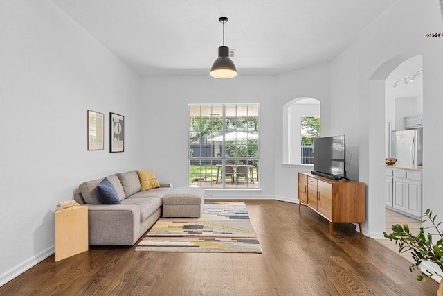 living room featuring arched walkways, baseboards, and wood finished floors