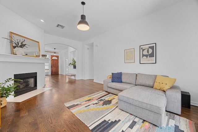 living room featuring arched walkways, baseboards, a fireplace with flush hearth, wood finished floors, and visible vents
