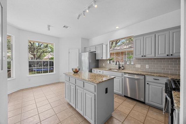 kitchen with appliances with stainless steel finishes, a sink, light tile patterned floors, a kitchen island, and visible vents