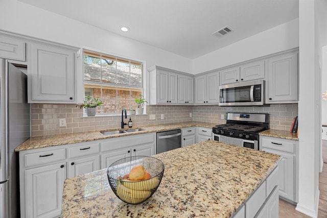kitchen featuring backsplash, visible vents, a sink, light stone counters, and stainless steel appliances
