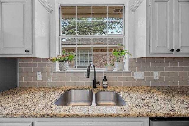 kitchen featuring visible vents, tasteful backsplash, light stone countertops, a sink, and white cabinets