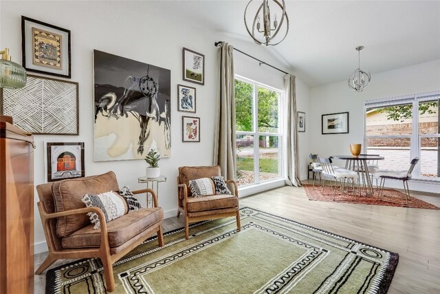 living area with a chandelier, plenty of natural light, wood finished floors, and lofted ceiling