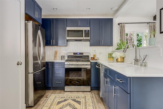 1415 Mearns Meadow Blvd, Austin, TX 78758 - kitchen with appliances with stainless steel finishes, a sink, blue cabinetry, and light wood-style flooring
