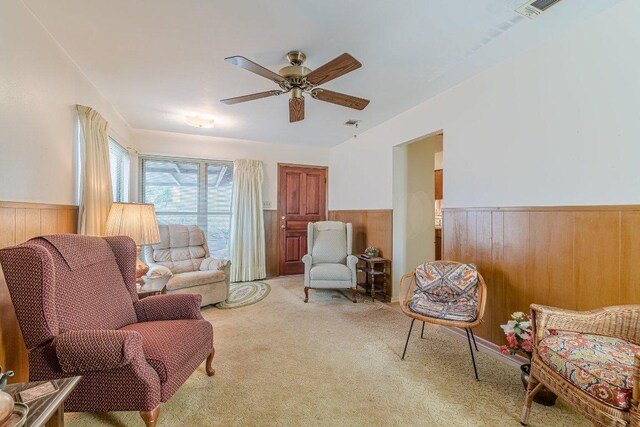 sitting room with wooden walls, ceiling fan, carpet, and wainscoting