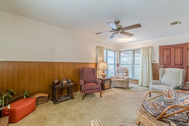 sitting room with light colored carpet, wood walls, visible vents, and a wainscoted wall
