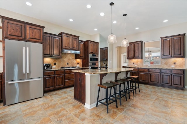 2420 Champions Corner Dr, Leander, TX 78641 - kitchen featuring stainless steel appliances, under cabinet range hood, decorative backsplash, a breakfast bar area, and dark brown cabinets
