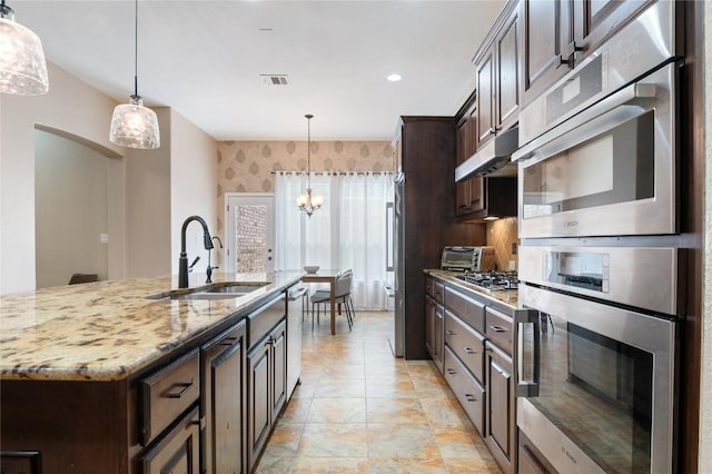 2420 Champions Corner Dr, Leander, TX 78641 - kitchen with dark brown cabinets, light stone counters, decorative light fixtures, a chandelier, and stainless steel appliances