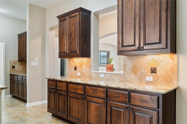 2420 Champions Corner Dr, Leander, TX 78641 - kitchen featuring tasteful backsplash, light stone countertops, arched walkways, and dark brown cabinetry