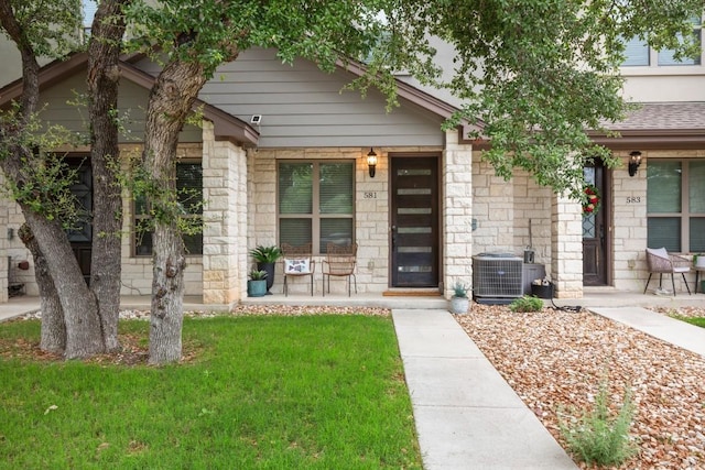 581 Demarett Dr, Point Venture, TX 78645 - view of front of property with covered porch, a front lawn, stone siding, central air condition unit, and roof with shingles