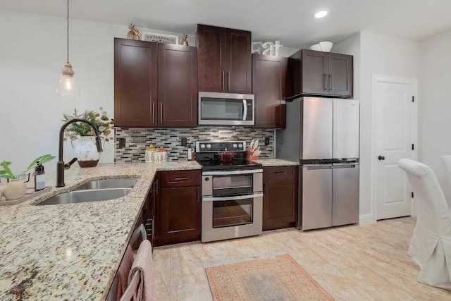 kitchen featuring dark brown cabinets, light stone countertops, a sink, stainless steel appliances, and backsplash