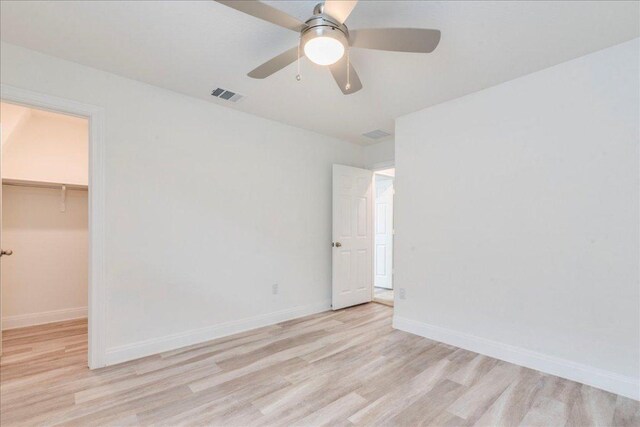 unfurnished bedroom featuring a walk in closet, baseboards, wood finished floors, and visible vents