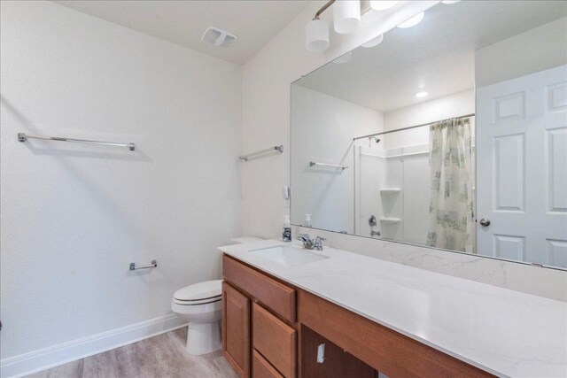 bathroom with toilet, a shower with shower curtain, baseboards, wood finished floors, and visible vents