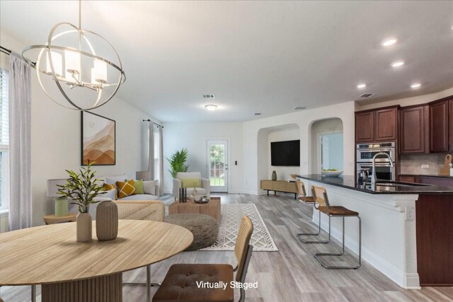 dining room featuring baseboards, recessed lighting, a chandelier, arched walkways, and light wood-style flooring
