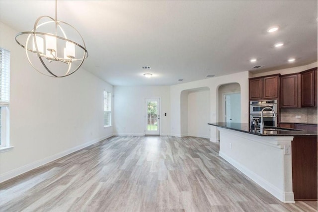 kitchen featuring an inviting chandelier, a sink, baseboards, arched walkways, and light wood-style flooring