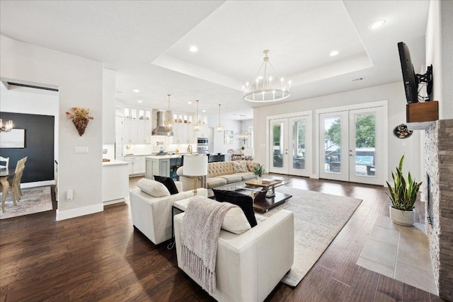 living room featuring an inviting chandelier, a raised ceiling, recessed lighting, and dark wood-type flooring