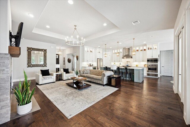living room featuring a raised ceiling, visible vents, recessed lighting, and a notable chandelier