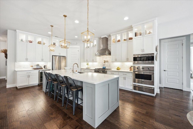 kitchen featuring wall chimney range hood, a sink, stainless steel appliances, backsplash, and a warming drawer