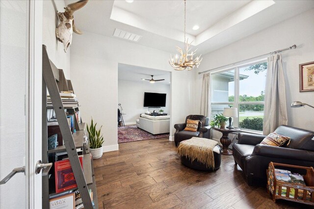 sitting room featuring a raised ceiling, ceiling fan with notable chandelier, hardwood / wood-style floors, baseboards, and visible vents