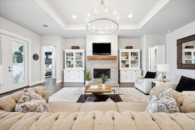 living room with dark wood-style flooring, a tray ceiling, a chandelier, and visible vents