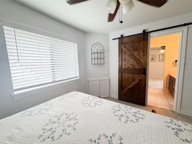 bedroom featuring light carpet, a ceiling fan, a barn door, and connected bathroom