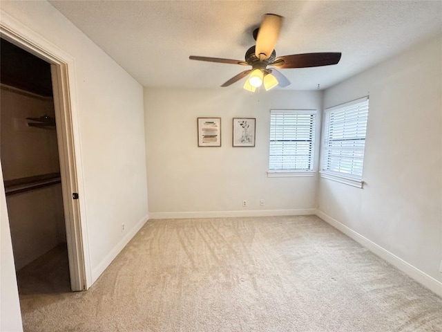 unfurnished bedroom with baseboards, a spacious closet, light carpet, and ceiling fan