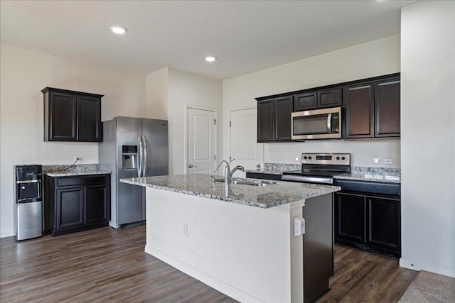 kitchen with light stone countertops, a center island with sink, dark wood-style floors, a sink, and stainless steel appliances