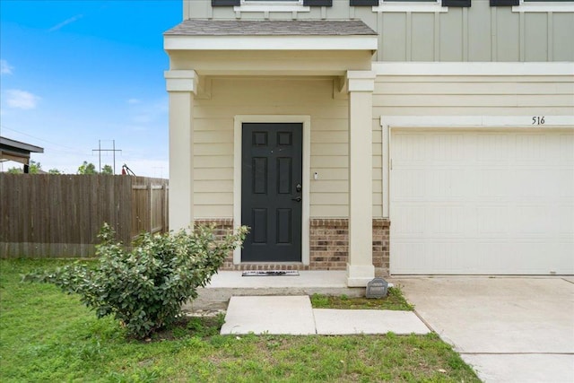 view of exterior entry with an attached garage, board and batten siding, fence, and driveway