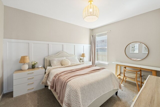 bedroom with carpet floors, a wainscoted wall, and a decorative wall