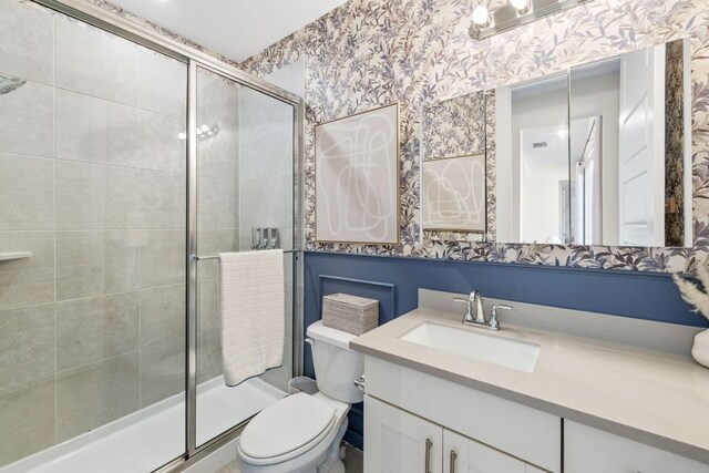 bathroom featuring vanity, toilet, wallpapered walls, and a stall shower